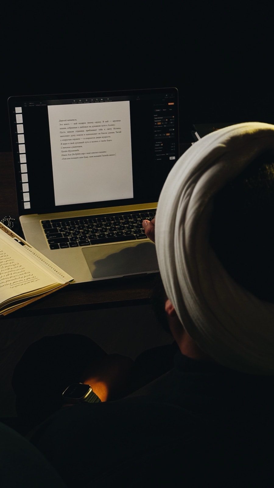 Учитель Хусейн за ноутбуком пишет слово читателю, рядом раскрытая книга